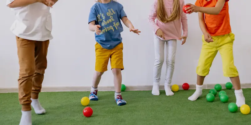 A group of children playing with colorful balls on artificial grass, wearing comfortable grip socks that provide stability and safety during active play.