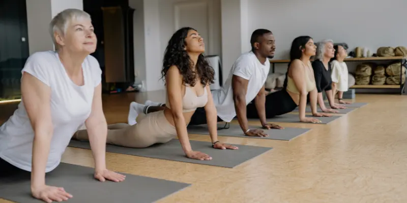 Group of diverse participants in a yoga class stretching in cobra pose on mats.